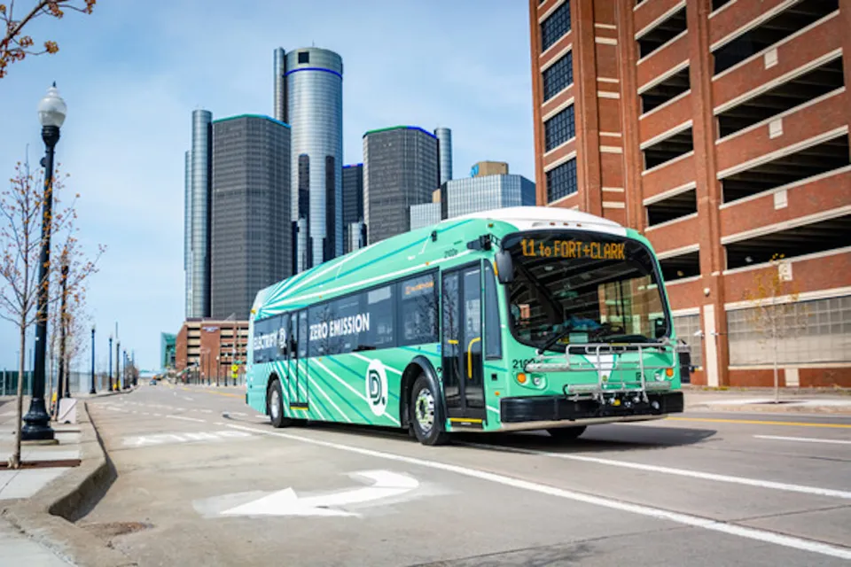 Green Detroit public transit electric bus with high-rise modenr building in background.